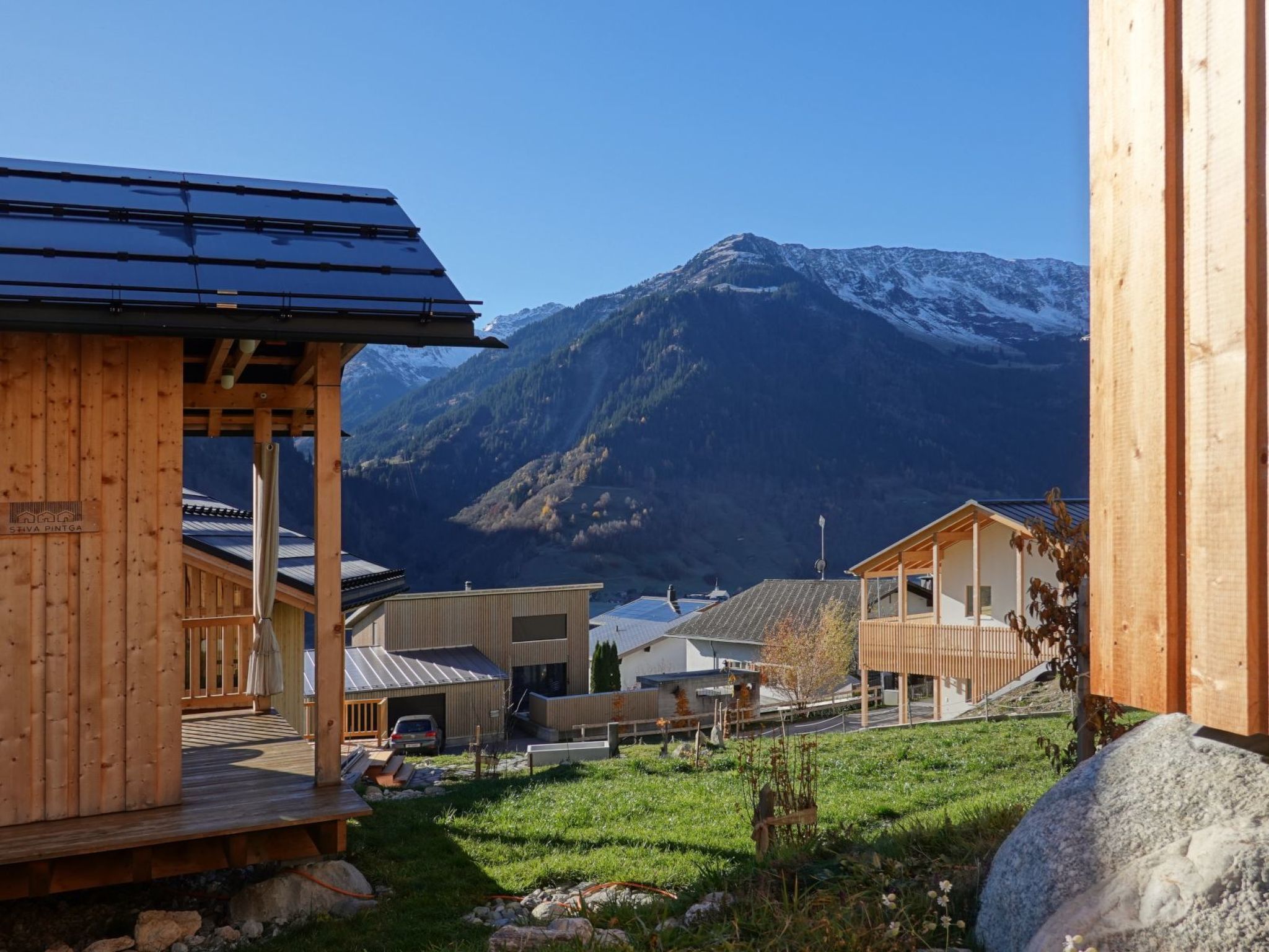 Eine Holzhütte mit einer Veranda, umgeben von einer Wiese und einem Berg im Hintergrund.