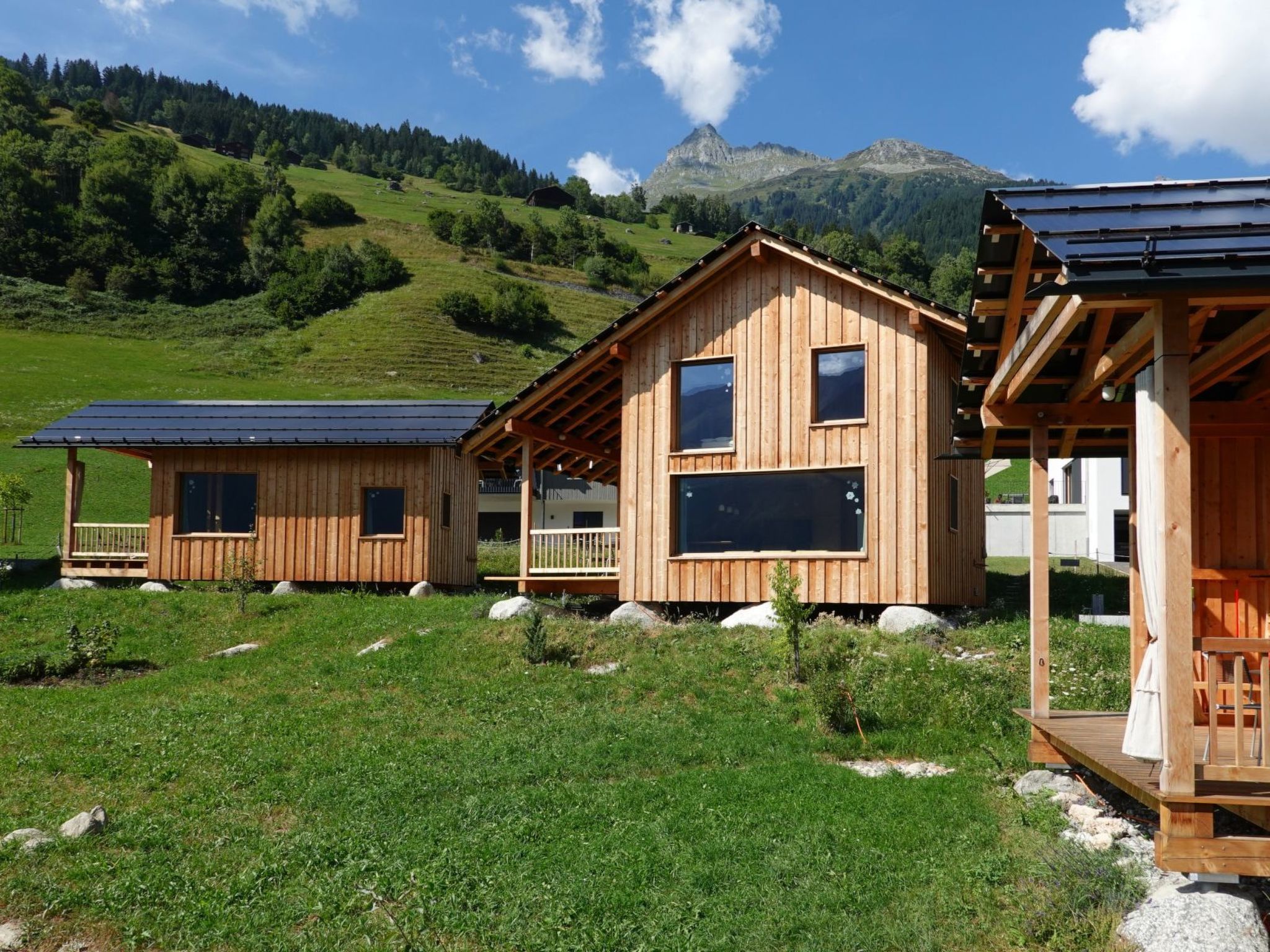 Eine Holzhütte mit einem Balkon, eingebettet in eine Wiese mit Bergblick.