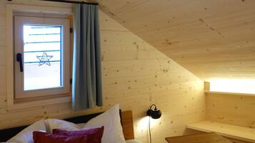 Ein Schlafzimmer mit Bett, Kissen, Nachttisch, Lampe, Fenster mit Vorhängen und einer Sterne-Dekoration.