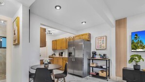 A modern kitchen with wooden cabinets, a stainless steel refrigerator, and a dining area with a round table and chairs. - Stylish 2BR & Parking in Design District (Miami)