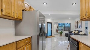 A modern kitchen with wooden cabinets, a stainless steel refrigerator, and a marble floor. - Stylish 2BR & Parking in Design District (Miami)