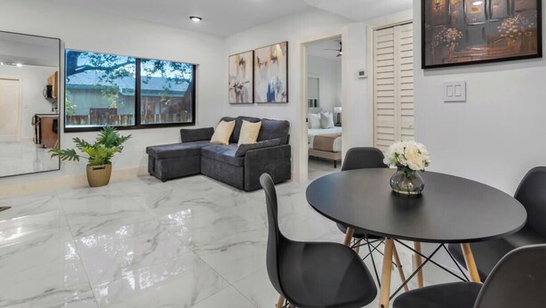 A modern living room with a sectional sofa, a dining table with chairs, and artwork on the walls. - Stylish 2BR & Parking in Design District (Miami)