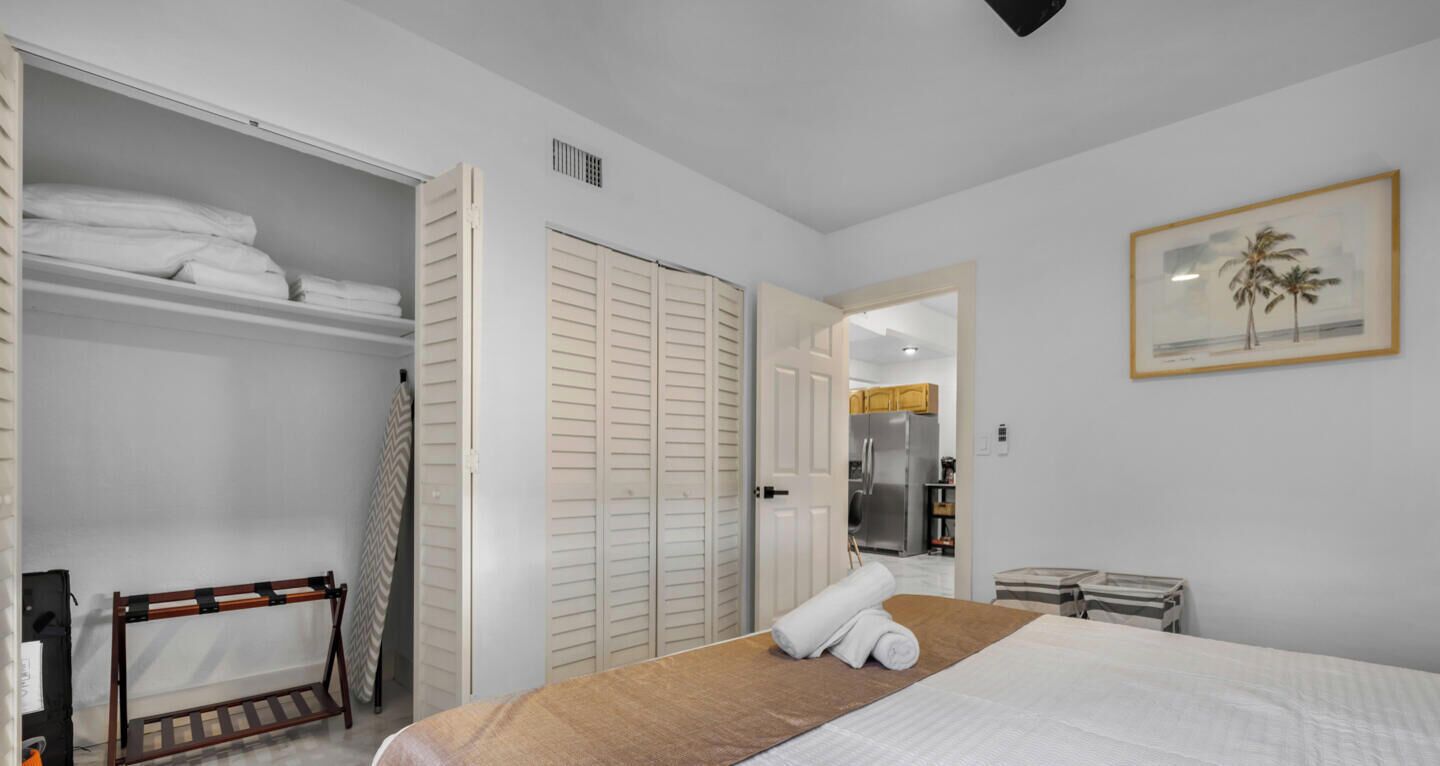 A hotel room with a bed, a wardrobe, a small table, and a painting on the wall.