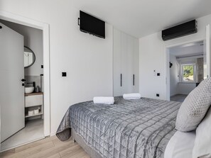 A modern bedroom with a bed, a TV, an air conditioner, and a bathroom with a sink and mirror. - Vacation home Marko by Interhome (Pirovac)