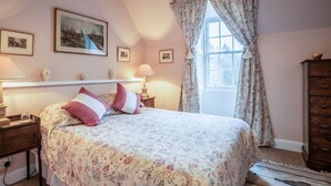 Une chambre à coucher comprenant un lit, une commode, une fenêtre avec des rideaux et des tableaux accrochés au mur.