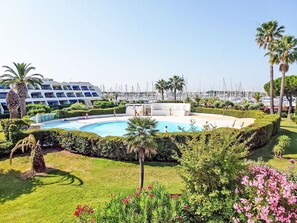 A resort with a swimming pool, palm trees, and a marina in the background. - Les Jardins du Port by Interhome (Port Camargue)