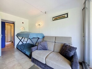 Ein kompakter Wohnraum mit einer Couch, einem Schlafsofa, einem gerahmten Bild und einer Tür zu einem Duschbereich.