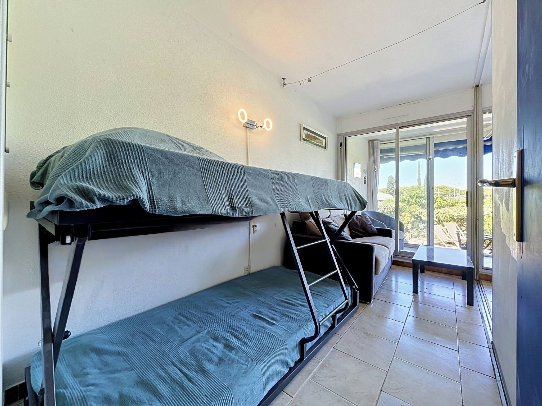 Quarto estilo dormitório com beliches, uma mesa pequena e uma janela com vista.