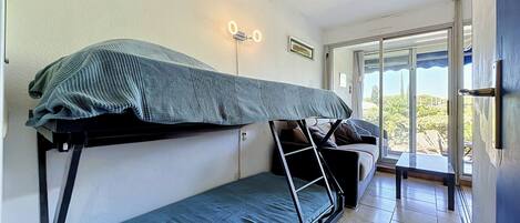 Habitación tipo dormitorio con literas, una mesita y una ventana con vistas.
