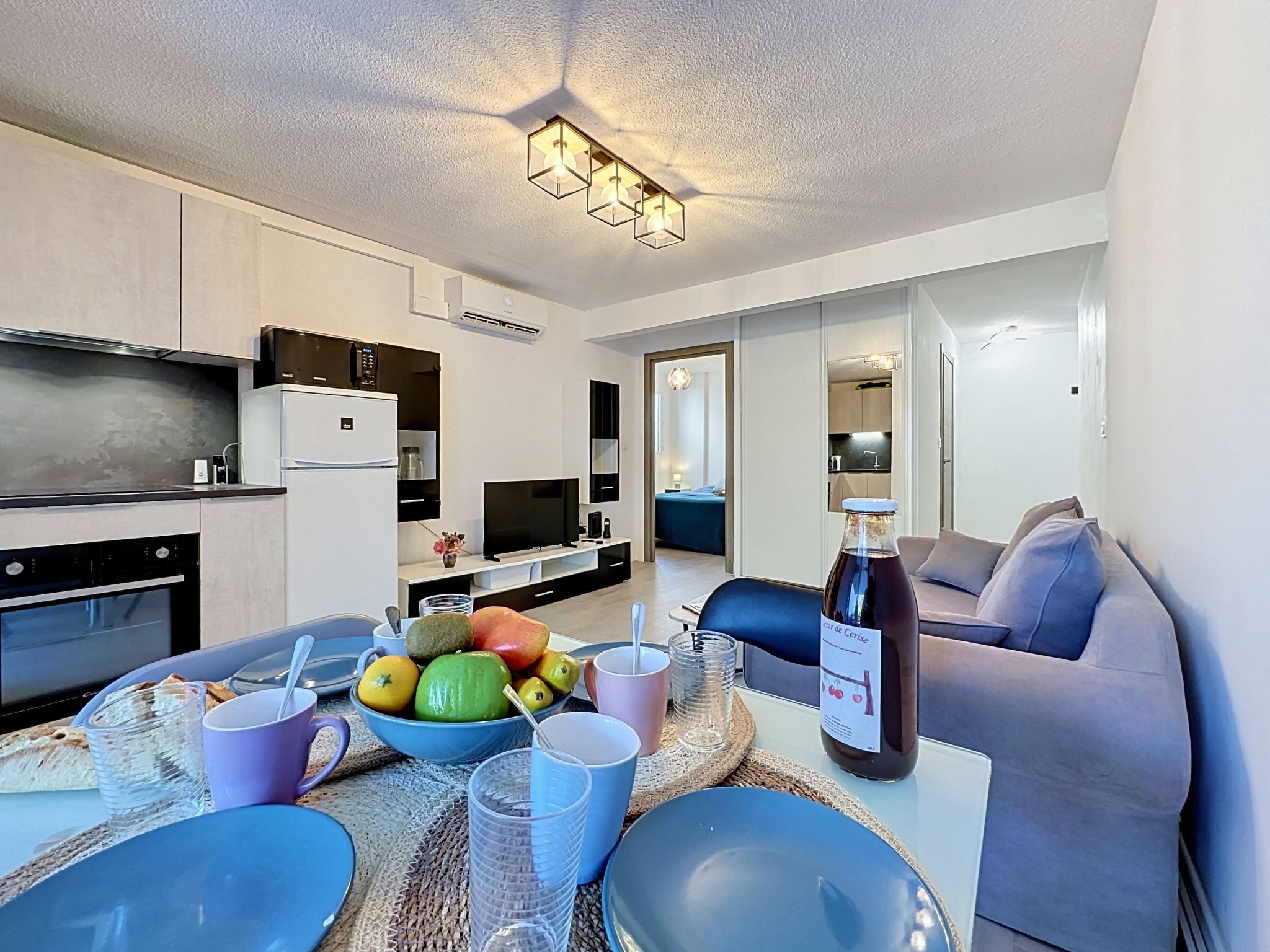 A modern living room with a dining area, a kitchen, and a separate bedroom.