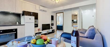 A modern living room with a dining area, a kitchen, and a separate bedroom.