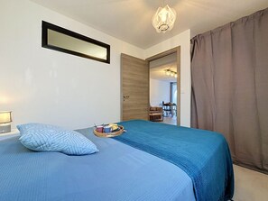 A bedroom with a bed, a bedside table, a mirror, and a view into the living area. - Dixie Land by Interhome (La Grande Motte)