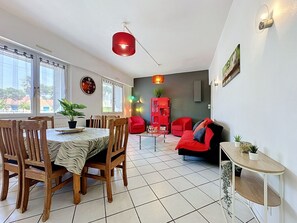 Ein Essbereich mit Holzkreisen und einem Tisch, ein Wohnzimmer mit roten Sofas und einem roten Schrank sowie eine Uhr an der Wand.