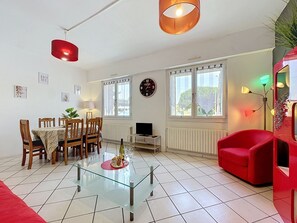 En stue med et glas sofabord, træstole, en rød sofa, et fjernsyn og en rød pendel.