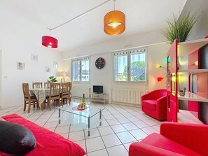 Ein Wohnzimmer mit Glastisch, roten Sofas, einem Essbereich mit Holzsesseln und einem roten Sessel.