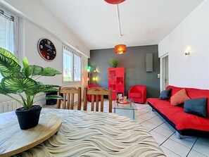 A modern living room with a red sofa, a wooden dining table with a potted plant, a red cabinet, and a wall clock. - L'Estuaire by Interhome (Saint Brevin les Pins)