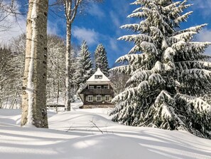 Eine verschneite Landschaft mit einer Holzhütte und schneebedeckten Bäumen.