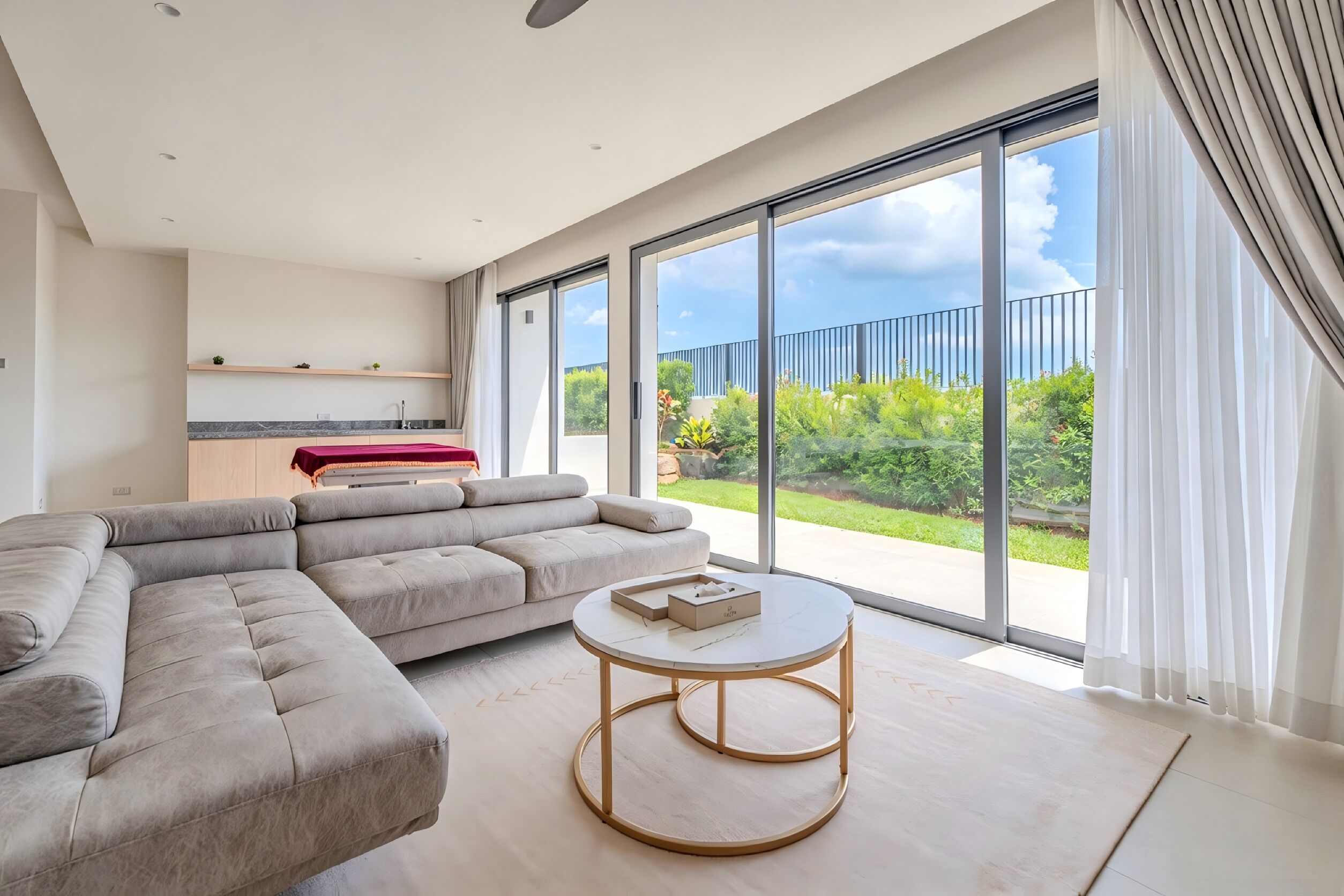 A modern living room with a sectional sofa, a round coffee table, and a view of the outdoors through large sliding glass doors.