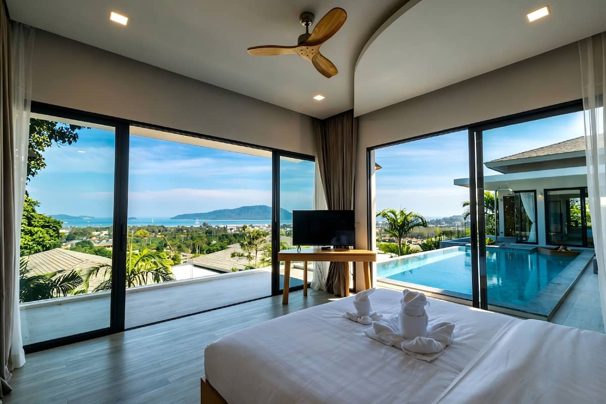 Ein modernes Hotelzimmer mit einem großen Bett, einem Fernseher und Blick auf einen Infinity-Pool.