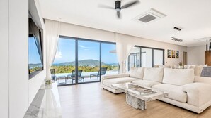 A modern living room with a large sofa, a marble coffee table, and a view of the ocean.