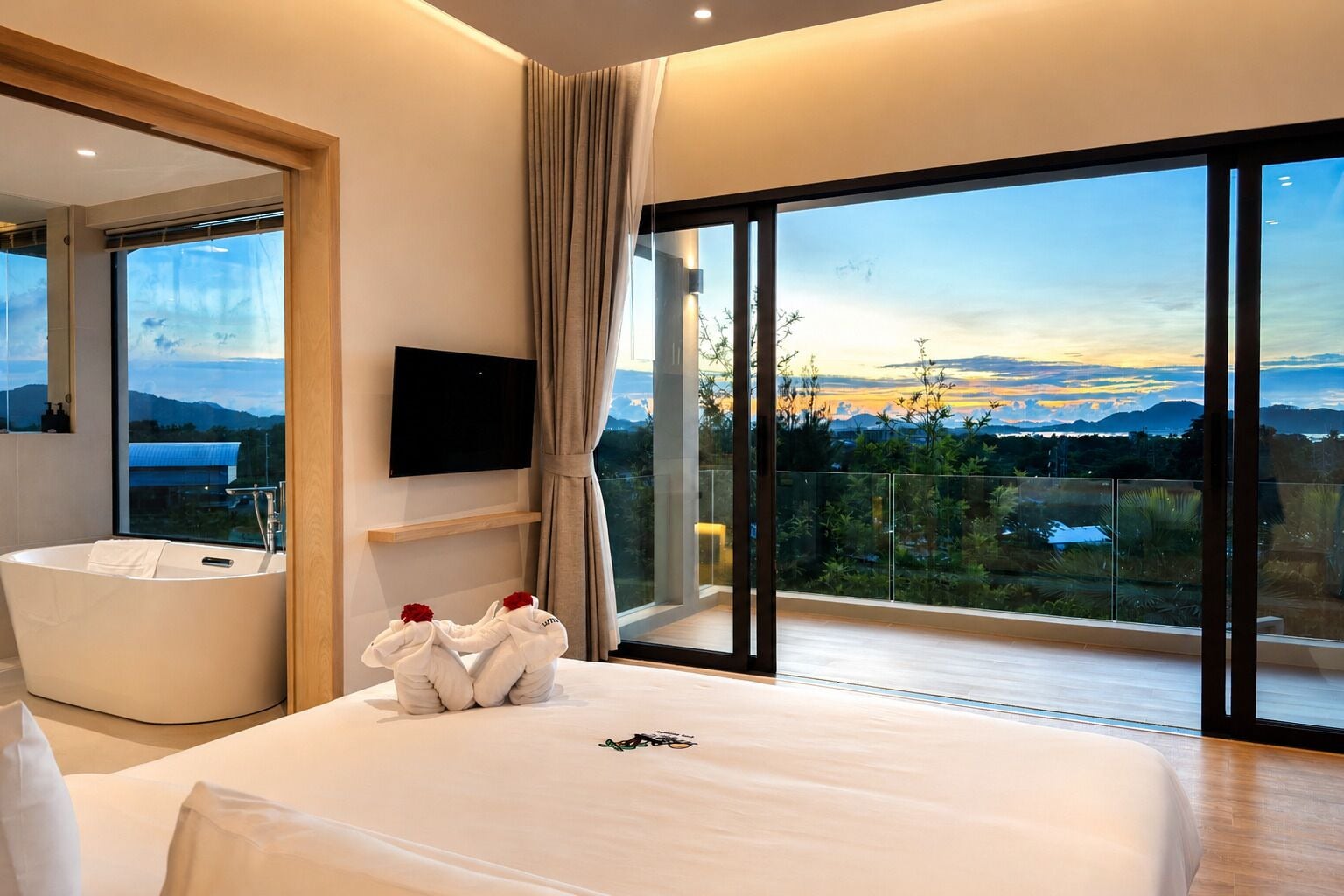 A modern hotel room with a large bed, a bathtub, a TV, and a balcony with a scenic view.