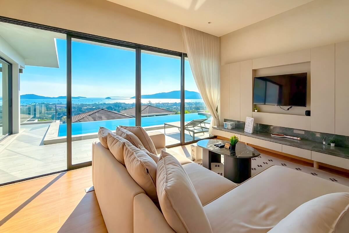 Ein modernes Wohnzimmer mit einer großen Couch, einem Flachbildfernseher und Blick auf einen Swimmingpool.