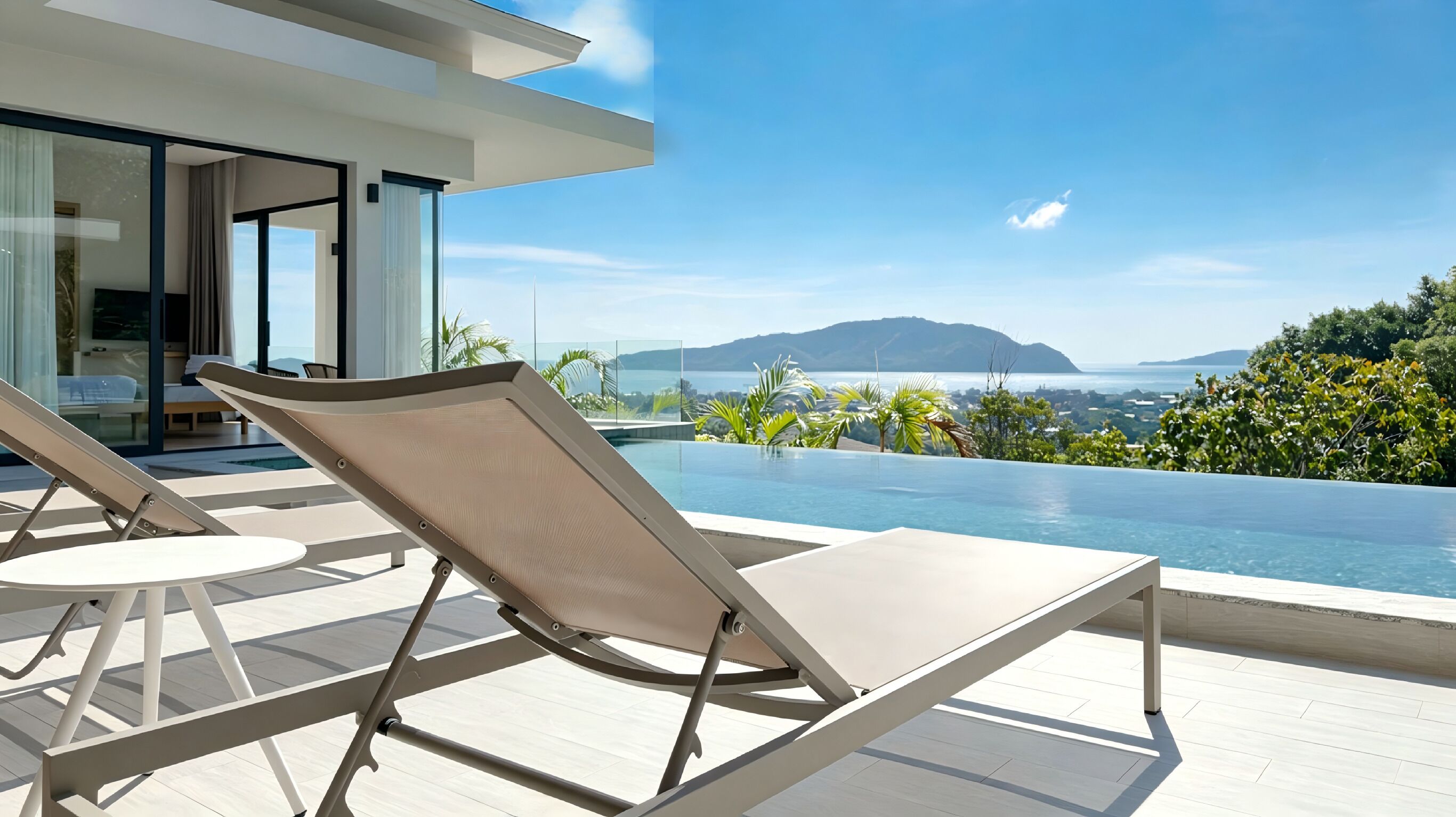 Un área de piscina moderna al aire libre con sillones de descanso, una sala con paredes de vidrio y vistas al mar y a las colinas.