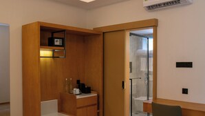 Habitación pequeña con un armario de madera, una mesita, una silla y un acceso de vidrio a la zona de la ducha.