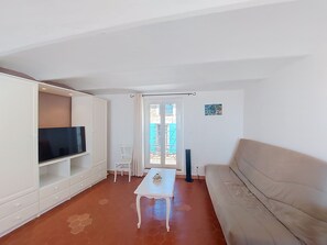 En stue med et fjernsyn, en hvid sofa, et lille bord og en stol.
