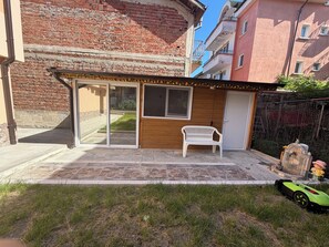 A building with a brick facade, a wooden door, a white bench, and a green toy car.