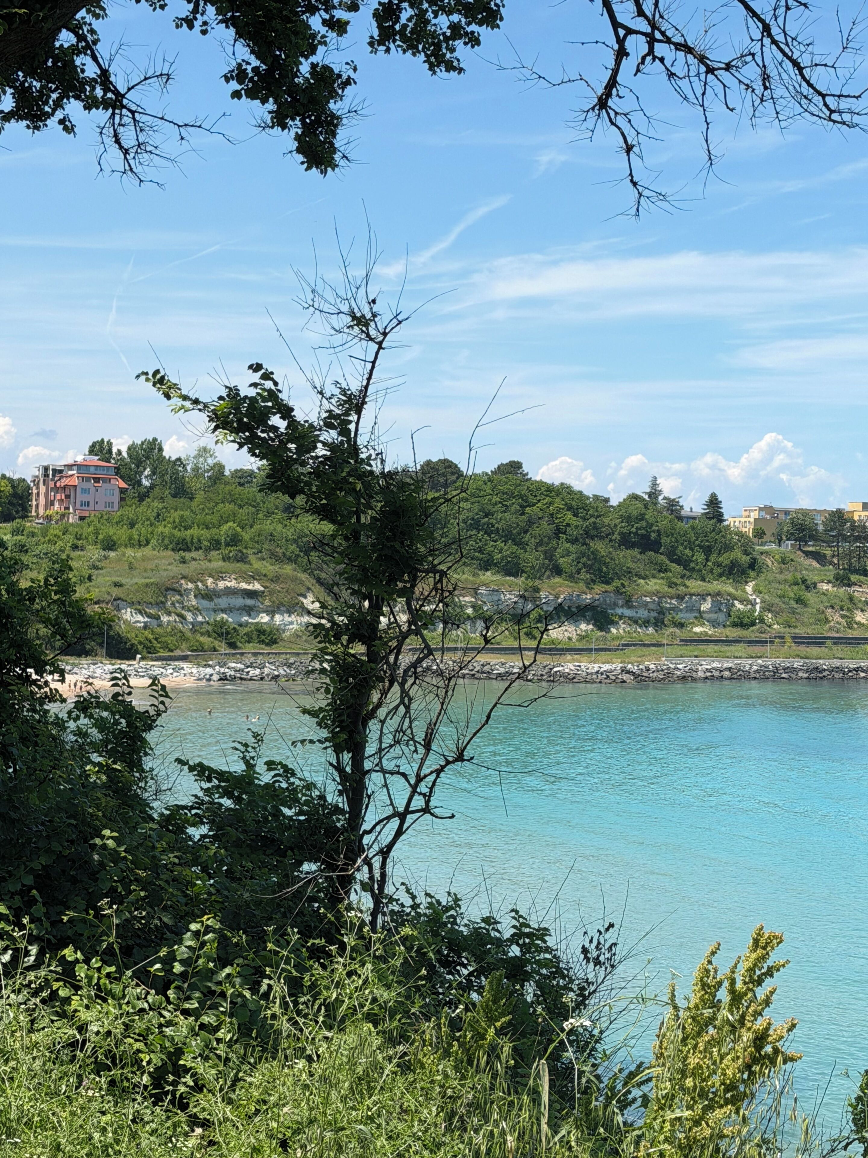 A coastal landscape with a clear view of the sea, a rocky shoreline, and a building in the background.