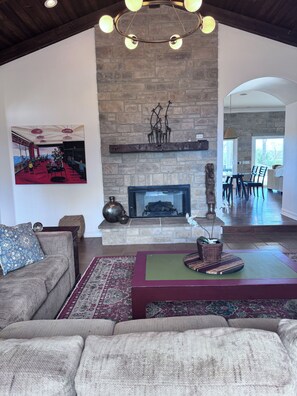 A spacious living room with a fireplace, a large painting, and a dining area visible through an open archway. - Tremendous 4-bedroom house in sunny Wine Country Temecula (Temecula)