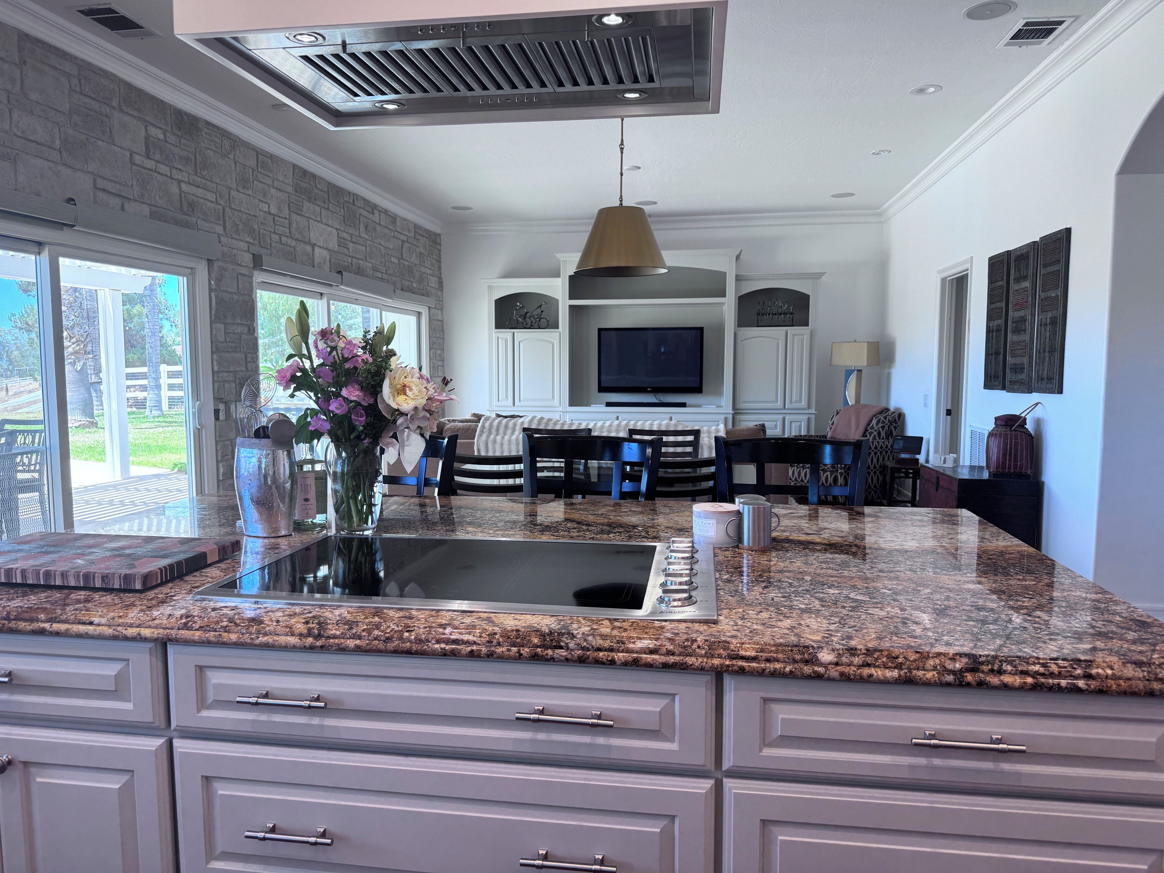 A modern kitchen with granite countertops, a built-in stove, and a dining area with a large TV.