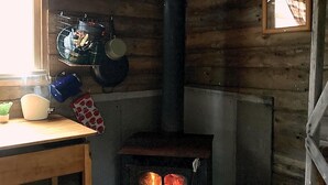 A rustic wooden interior with a wood-burning stove, a window, and a table with kitchen items. - Spruce, the tiny cabin in the woods (Markdale)