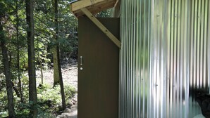 A rustic wooden structure with a metal door, surrounded by a forested area. - Spruce, the tiny cabin in the woods (Markdale)