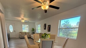 A spacious living room with a dining area, a ceiling fan, and a large window.