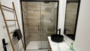 Une salle de bain équipée d’une douche, d’un lavabo, d’un miroir et d’un porte-serviettes.