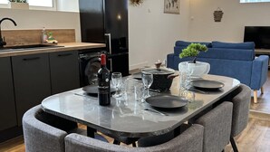 Une cuisine moderne avec une table à manger pour deux, un réfrigérateur noir et un canapé bleu dans l’espace salon.
