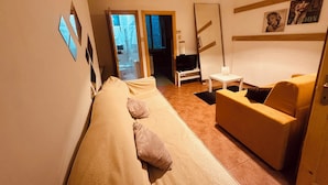 A room with a sofa, a chair, a small table, a TV, and a mirror.