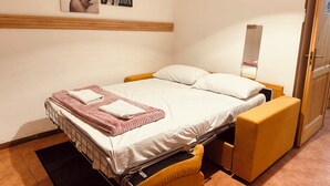 A single bed with a headboard, a bedside table, a mirror, and a wall-mounted clock.