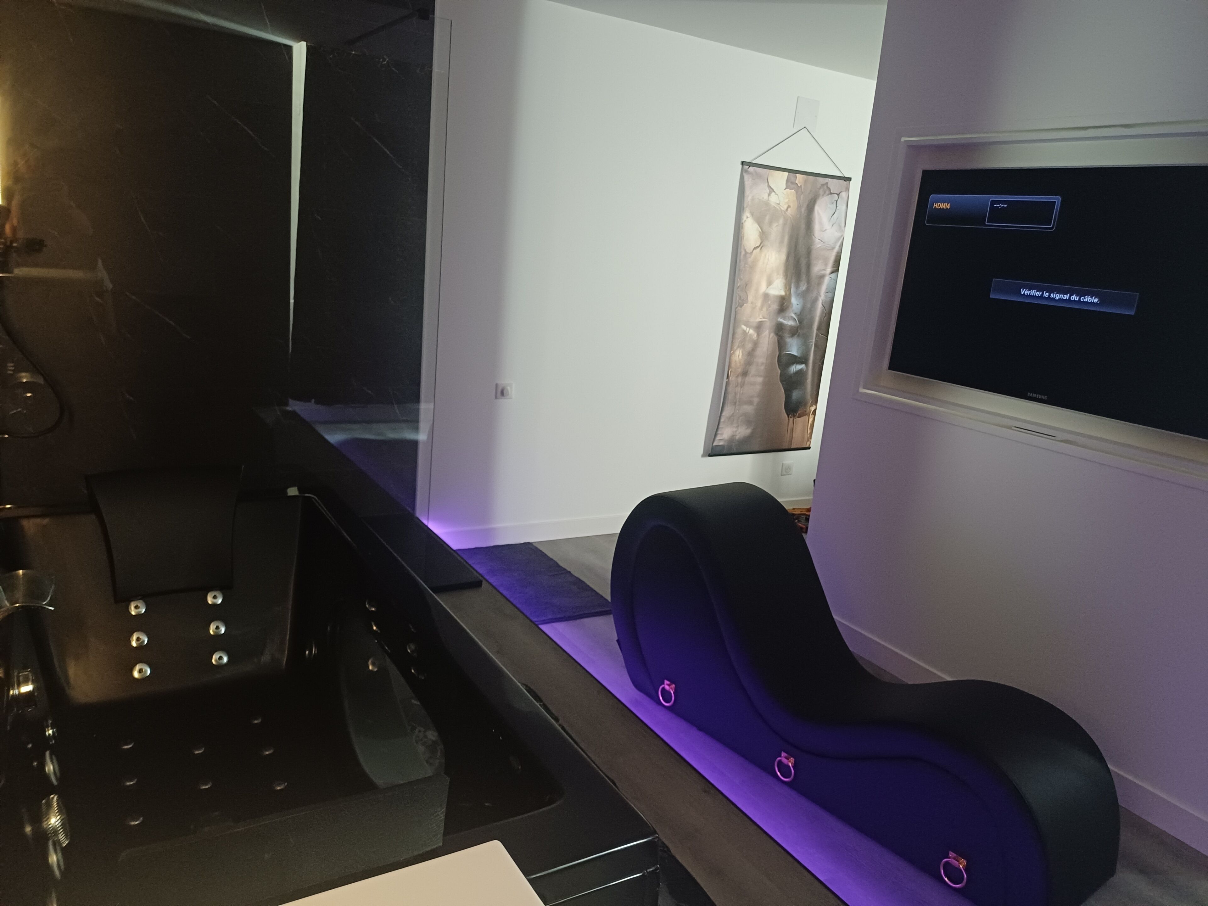 Een moderne kamer met een flatscreen televisie aan de muur, een zwarte bank met paars accent en een glazen scheidingswand.