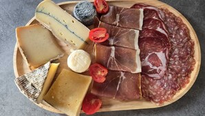A wooden board with various cheeses, cured meats, and a small round cheese.