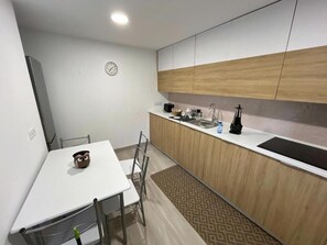 A compact kitchen with a white countertop, wooden cabinets, a sink, and a clock on the wall.