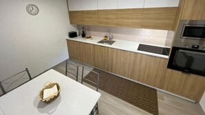A modern kitchen with a white countertop, wooden cabinets, a built-in oven, and a clock on the wall.