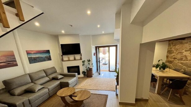 A modern living room with a sofa, a coffee table, and a fireplace. There is a dining area with a table and chairs.