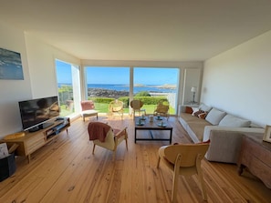 Ein geräumiges Wohnzimmer mit großem Fernseher, Holzböden und Meerblick.