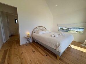 Ein Schlafzimmer mit Bett, Nachttisch mit Lampe, Fenster mit Blick und Holzboden.