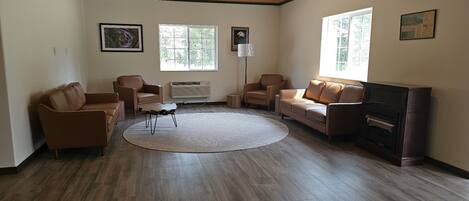 A spacious living room with a wooden ceiling, large windows, a fireplace, and leather sofas.