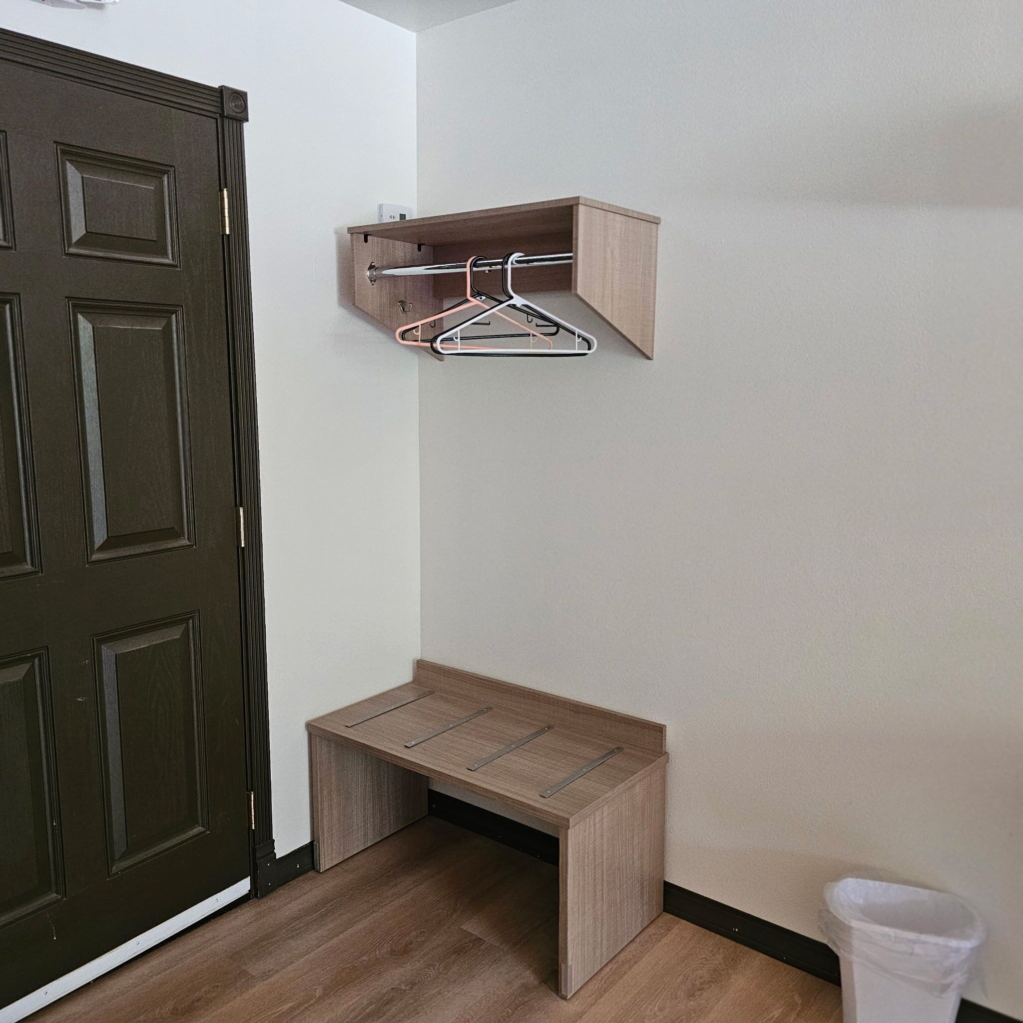 Una habitación de esquina con una puerta de madera oscura, un pequeño banco de madera y un perchero de pared.