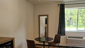 A room with a dining table, two chairs, a microwave, a wooden cabinet, a mirror, a window with curtains, and an air conditioning unit. - The Coolin Motel (Coolin)